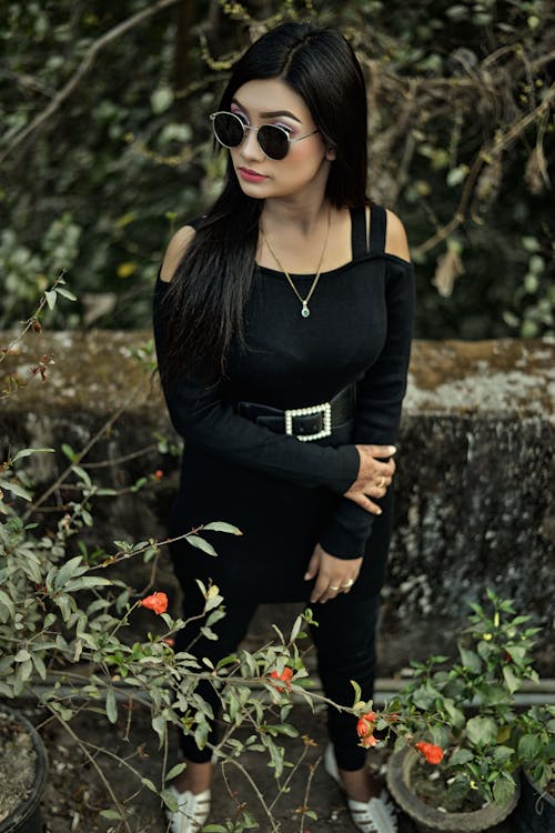 Woman in Black Dress Standing Beside Concrete Wall in Trees
