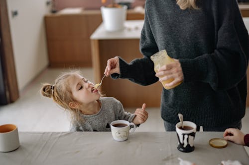 Free Woman Holding a Jar While Feeding a Girl with Honey Stock Photo