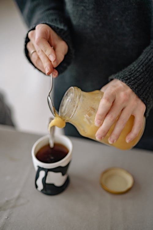 Free Woman Holding a Jar and Putting Honey into Tea Cup Stock Photo