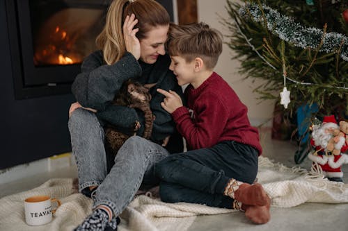 Mother Holding a Cat with her Son Sitting by the Fireplace at Christmas 