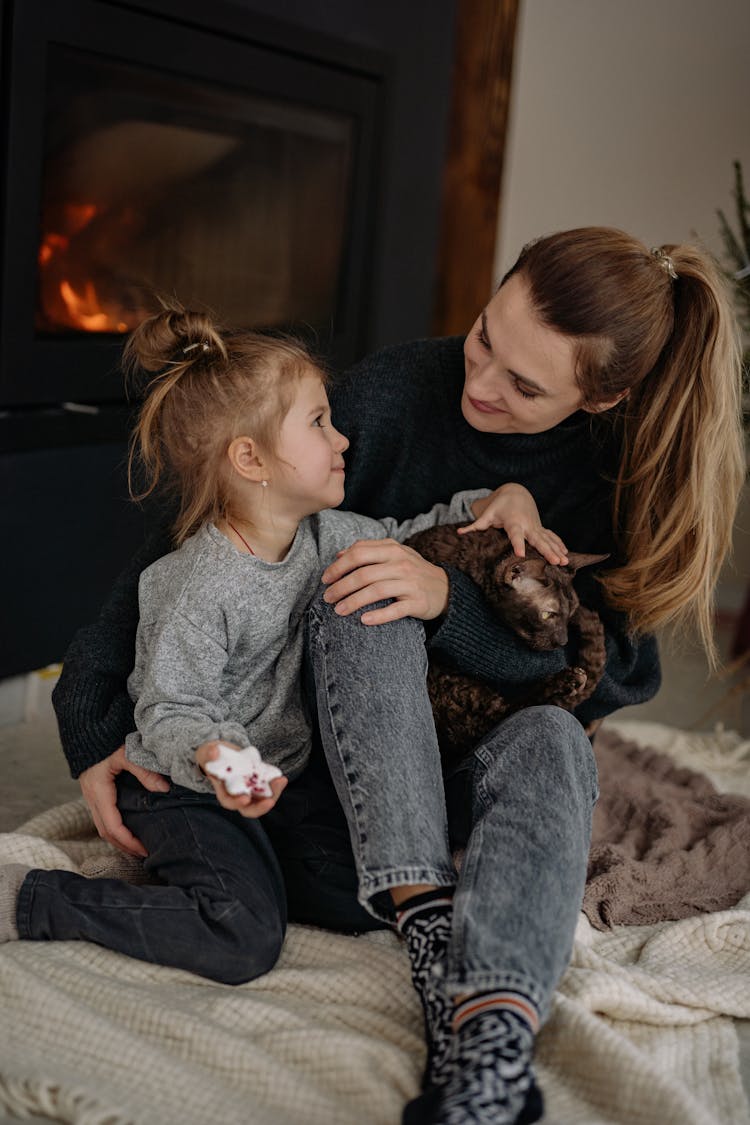 Woman Sitting With Her Daughter On A Bed And Fireplace In Background