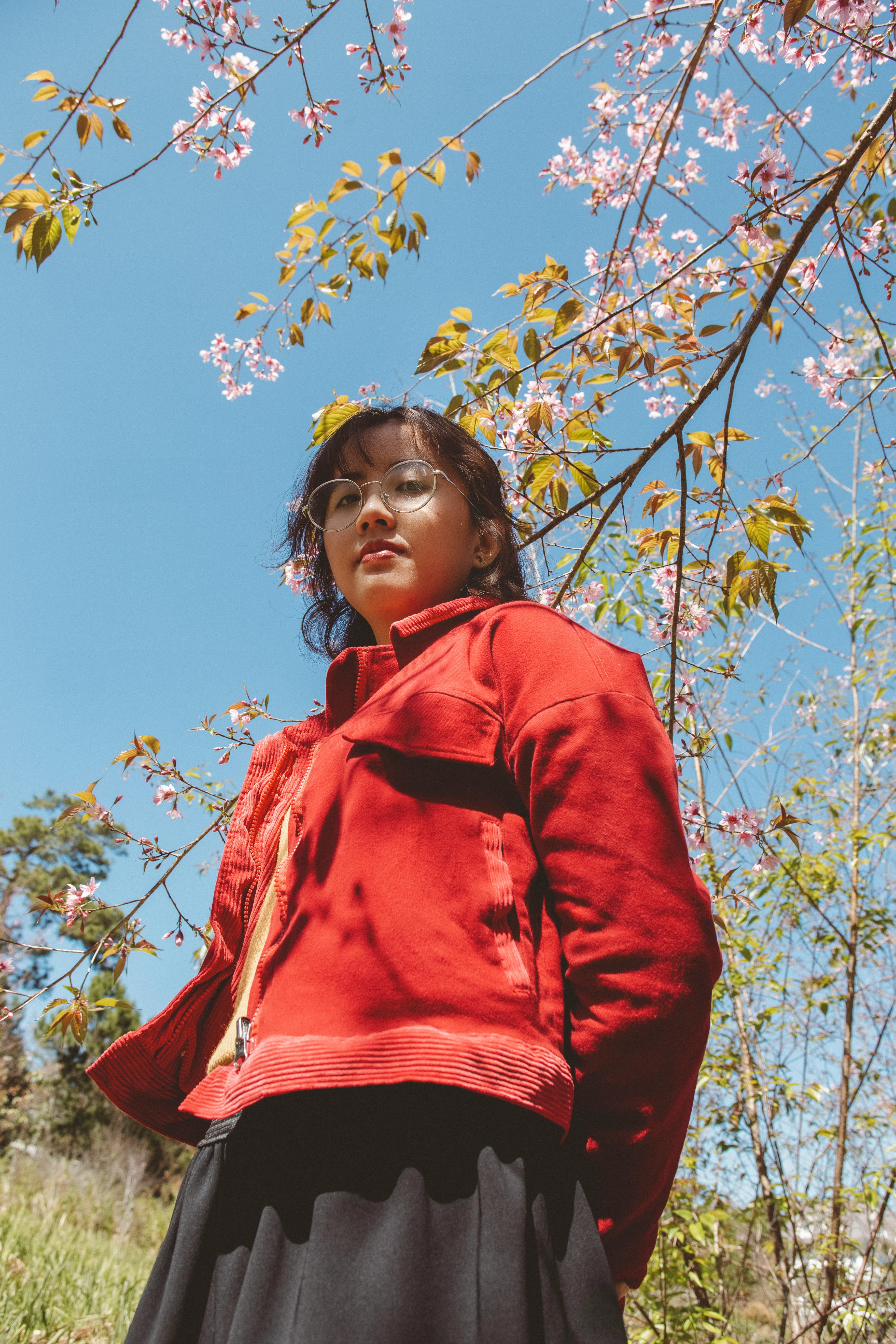 portrait of young woman in red jacket under tree in blossom