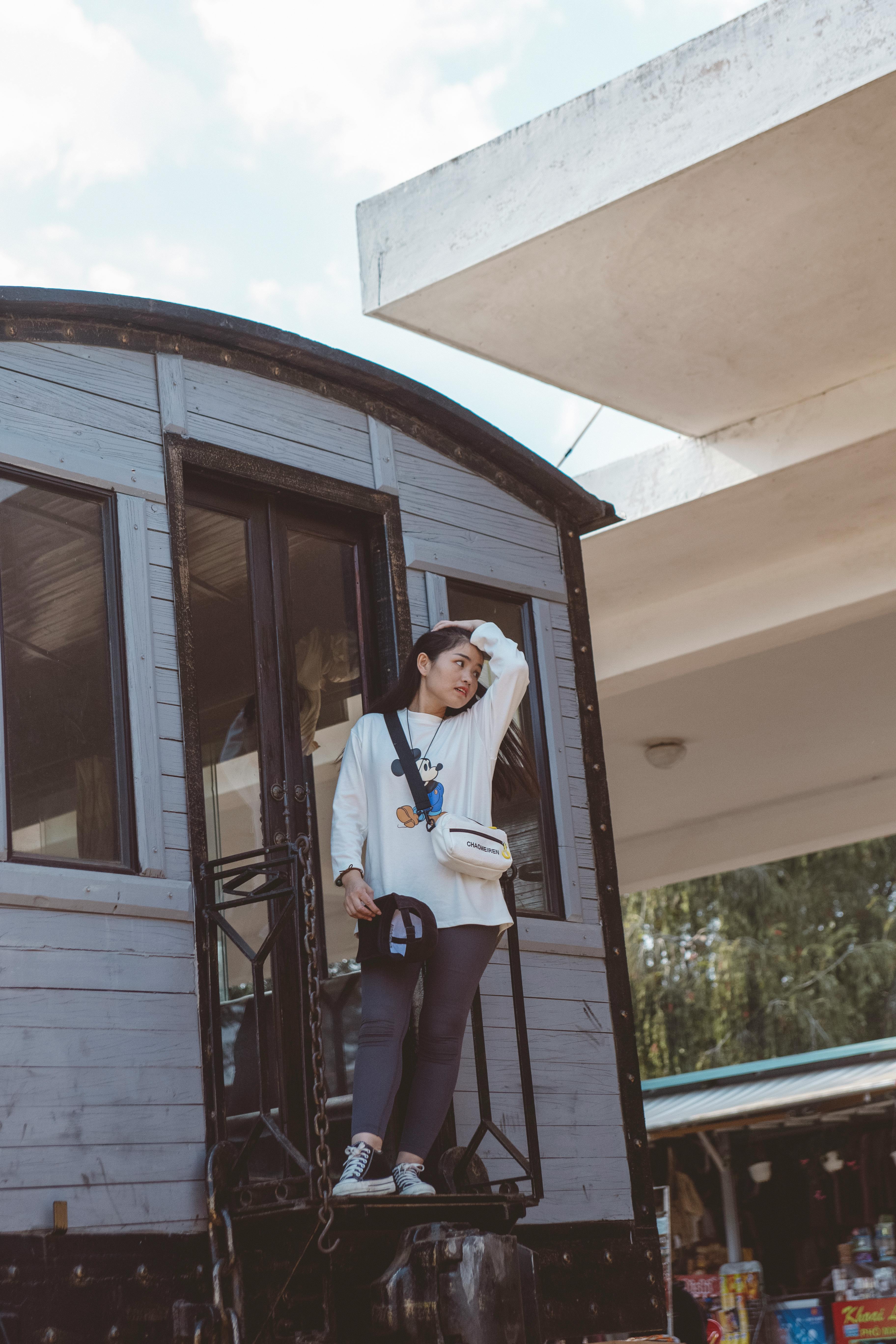 Free Young woman standing on a vintage train carriage outdoors, enjoying a sunny day. Stock Photo