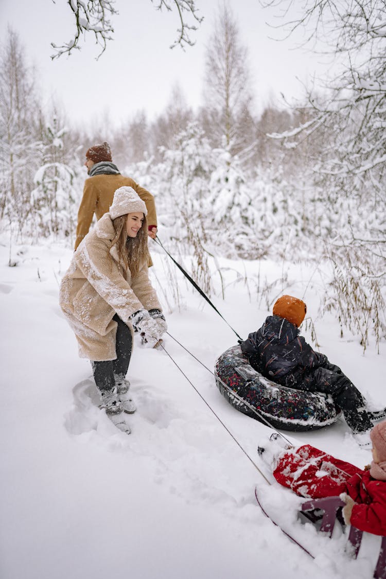 Family With Children Walking In Snow With Sledges