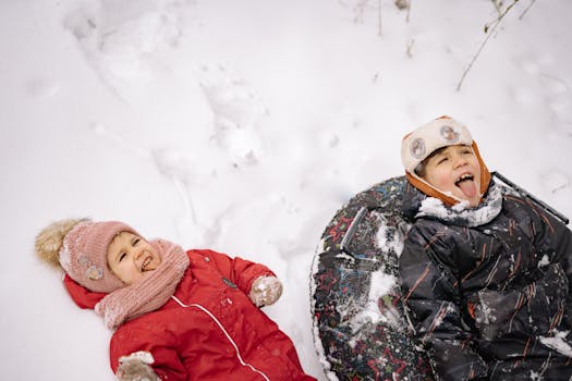 Two children having fun in the snow, dressed warmly in winter clothing.