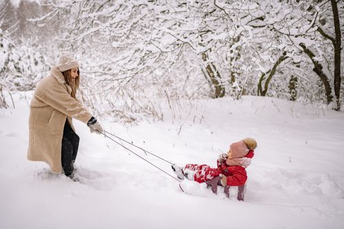 Free Woman pulling child on a sled in a snowy winter landscape, enjoying outdoor fun. Stock Photo