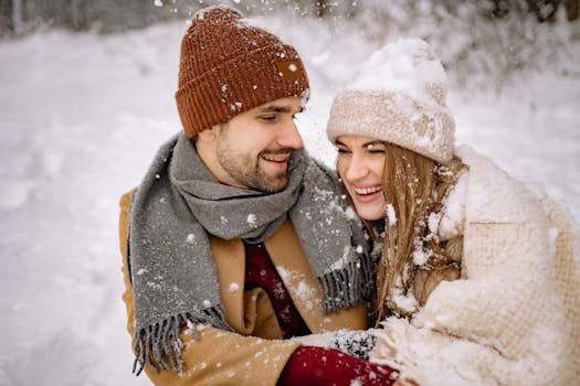 A happy couple in cozy winter attire embracing joyfully amidst a snowy landscape.