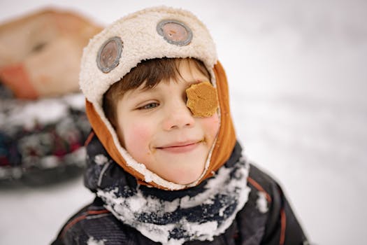 Smiling boy wearing a winter hat playfully posing with a biscuit on his eye.