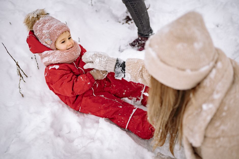 Child enjoying a playful moment in the snow, dressed warmly in winter clothes, with family nearby.