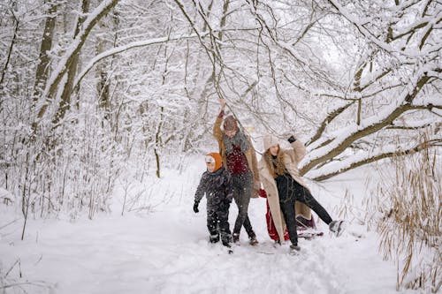 A Family in Winter Clothes Walking on a Snow-Covered Ground near the Tree Branches