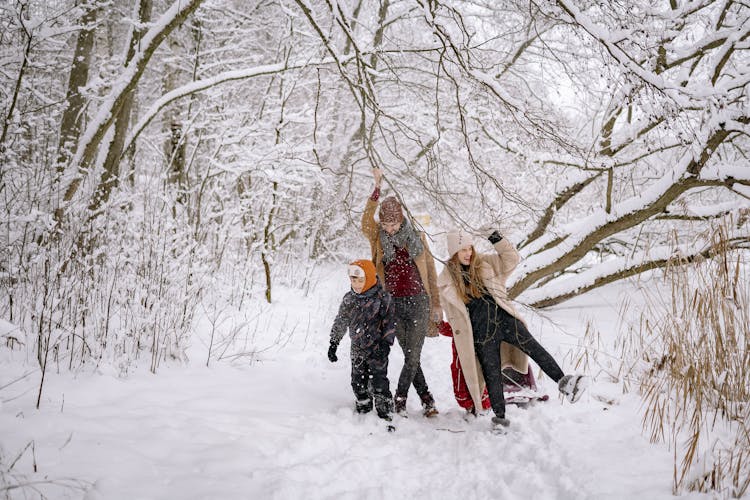 A Family In Winter Clothes Walking On A Snow-Covered Ground Near The Tree Branches