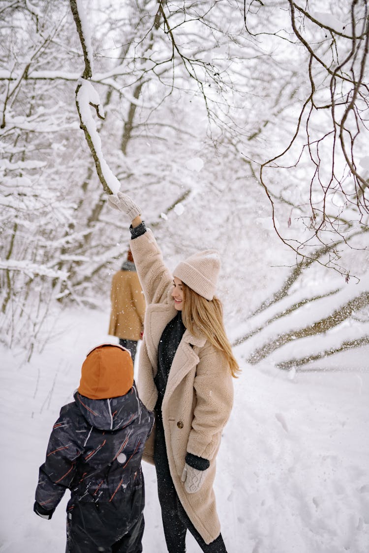 A Mom And Child In Winter Clothes Reaching The Tree Branch