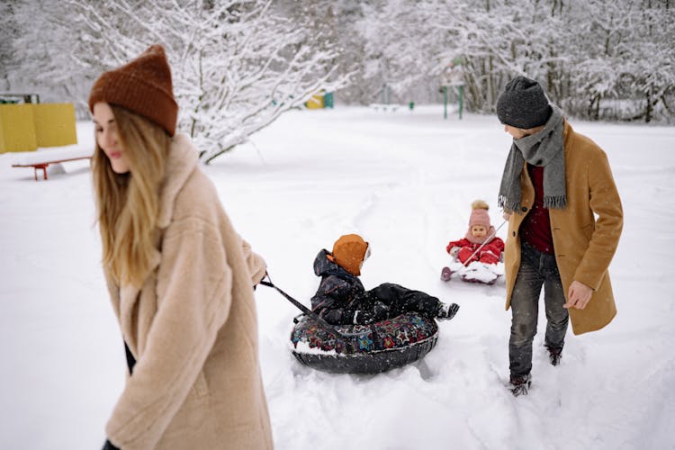 A Couple Pulling Snow Tubes On The Snow With The Kids