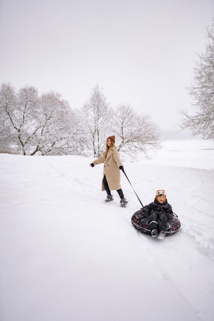 A mom enjoying winter with her child on a sled in a snowy park.