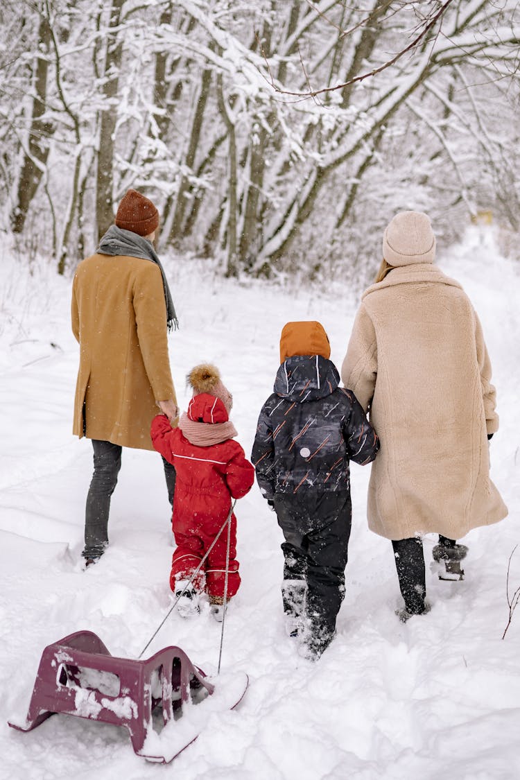 Back View Of A Family In Winter Clothes Walking On A Snow-Covered Ground