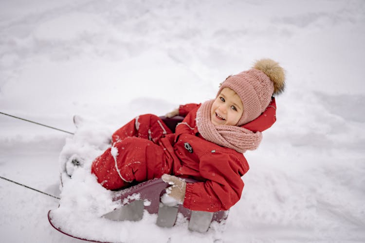 A Cute Girl In Winter Clothing Riding A Sledge