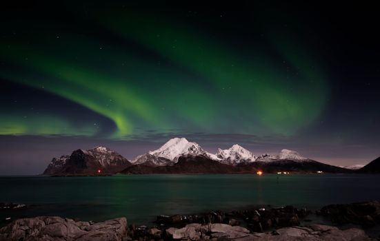 Capture of the Northern Lights dancing over snow-covered mountains and a scenic lake.