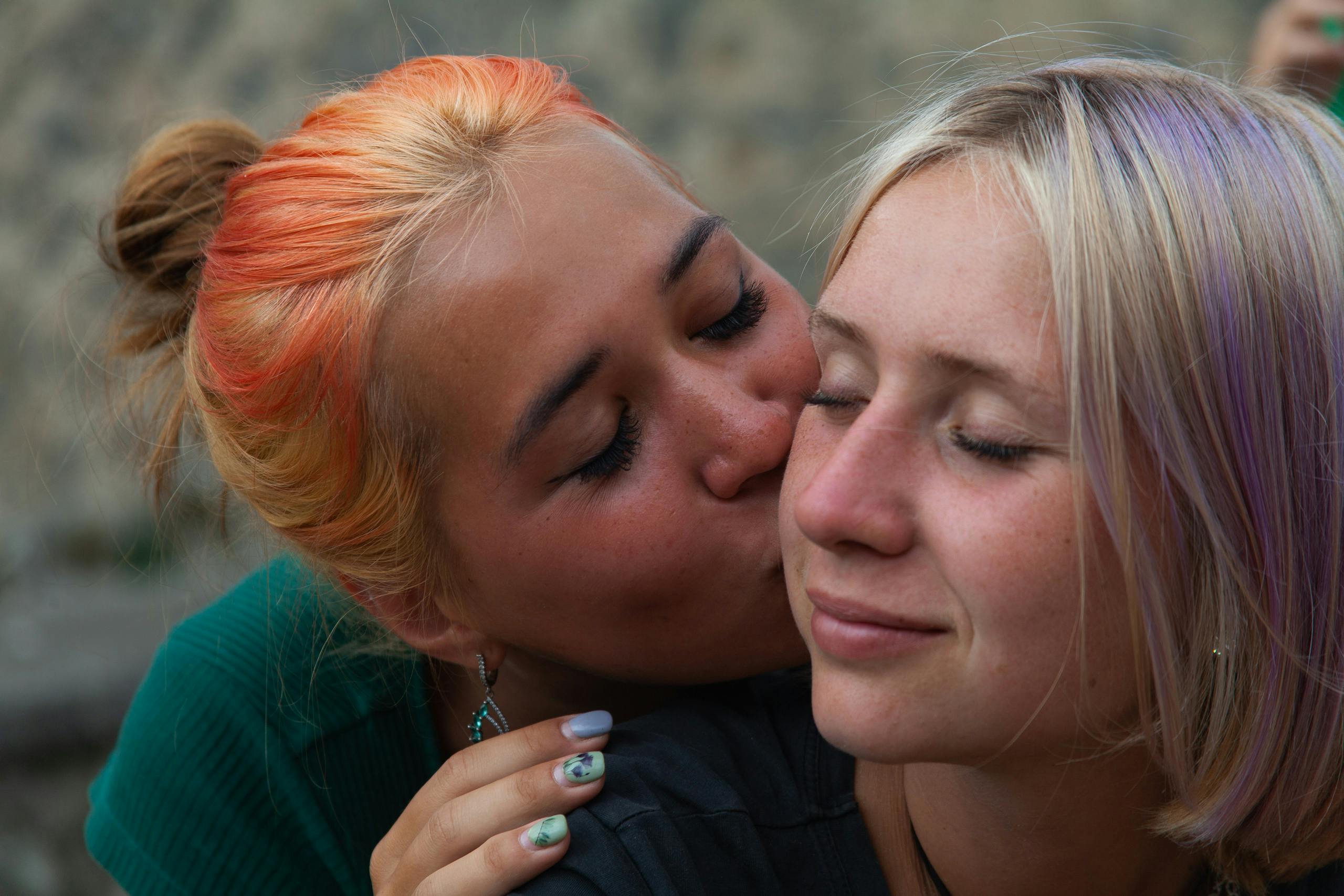 close up of a woman with dyed hair kissing a woman on a chick