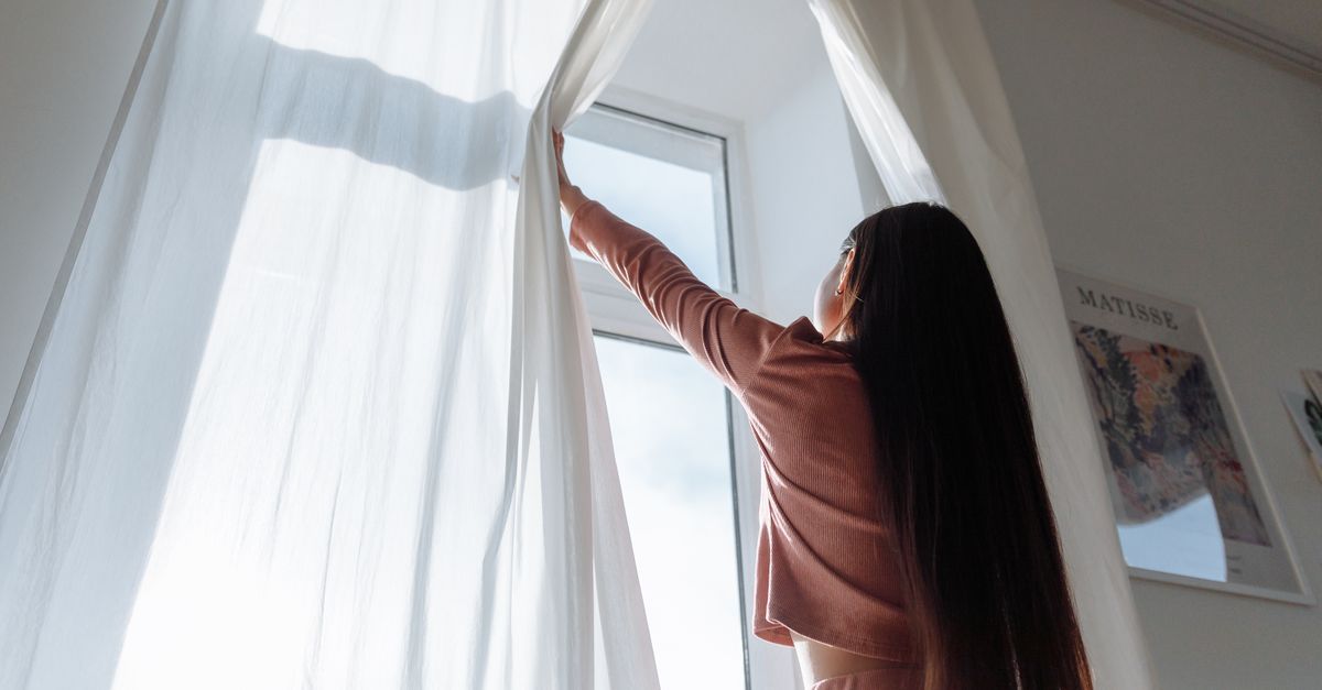 Vrouw opent witte vitrages voor een zonnig raam