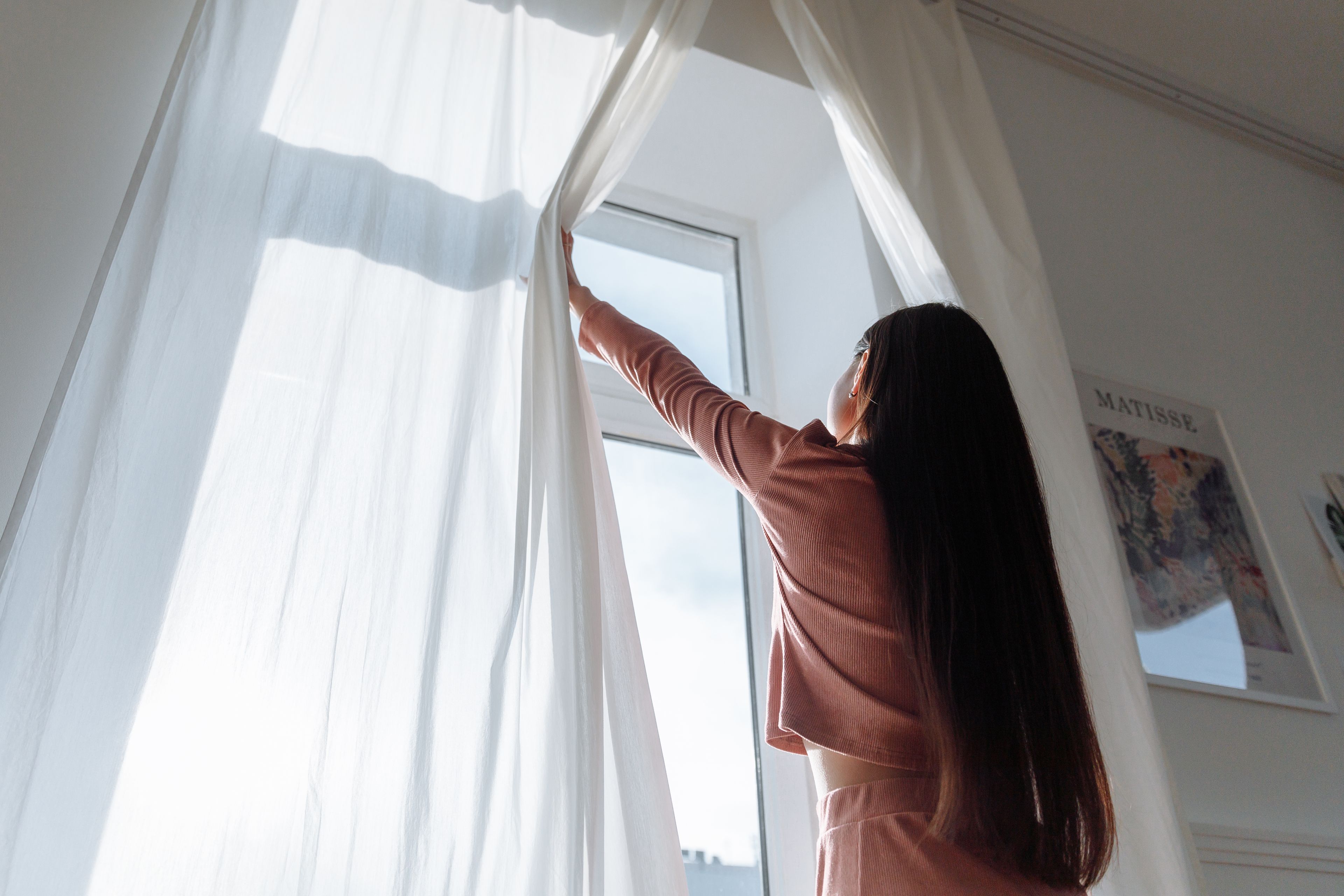 Rideau blanc écarté devant une fenêtre ouverte laissant entrer la lumière du jour