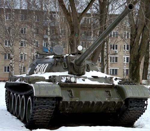 Free Front view of a military tank in an outdoor snowy environment surrounded by trees and buildings. Stock Photo