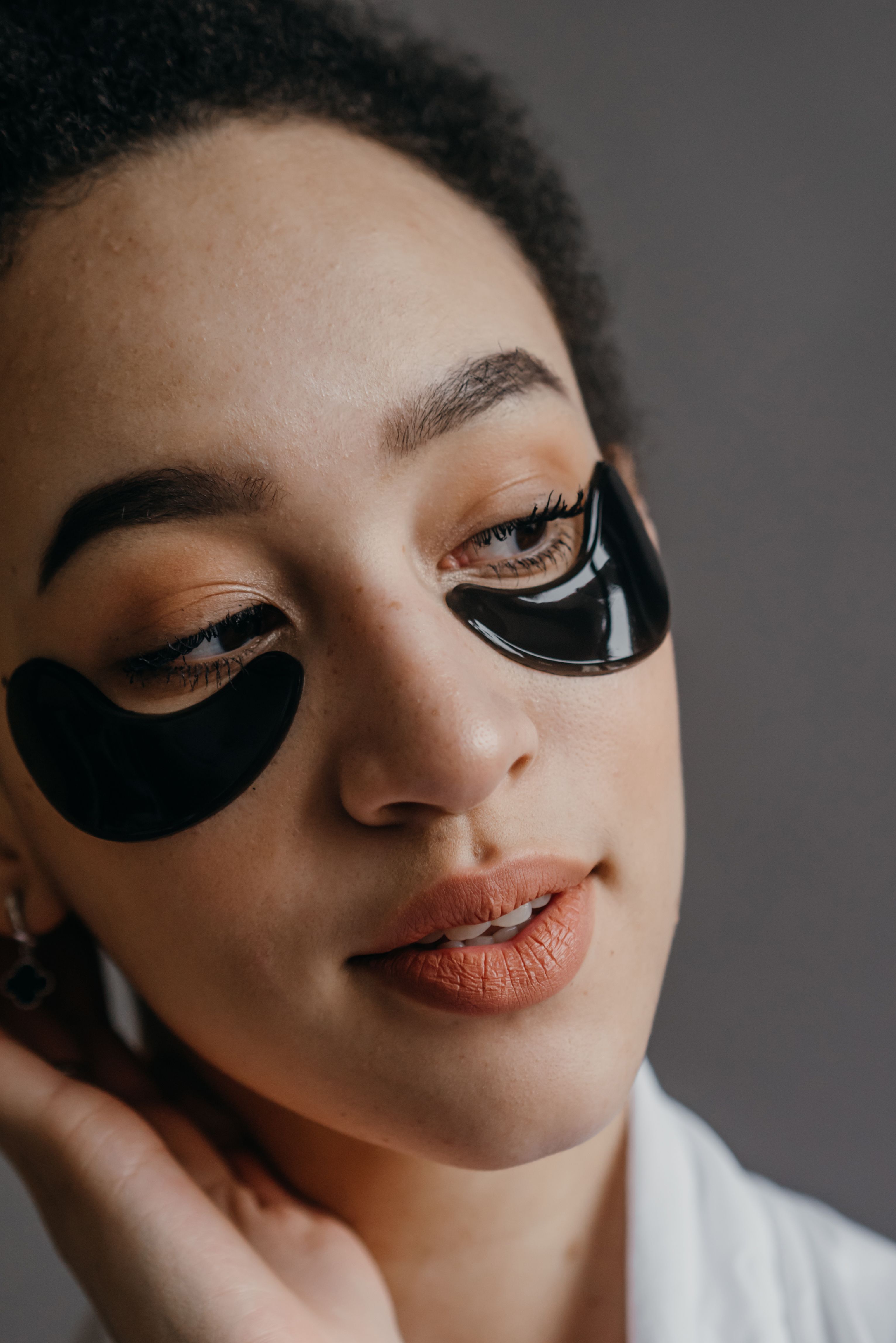 A close-up portrait of a woman wearing black under-eye masks for skincare.