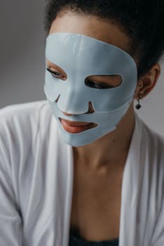 A woman wearing a skincare face mask and earrings in a serene indoor setting.