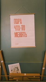Motivational poster with Cyrillic text hanging on a green wall indoors.
