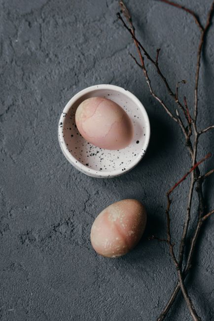 Still life photograph of pink eggs on a speckled plate with twigs, creating a rustic aesthetic.