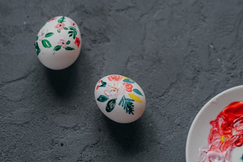 Top view of white chicken eggs decorated with painted colorful floral ornament laced in rough gray table during Easter preparation