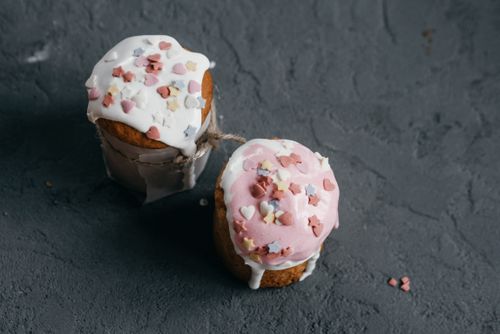 Free Top-down view of two Easter cupcakes decorated with colorful heart and star sprinkles on a textured concrete background. Stock Photo