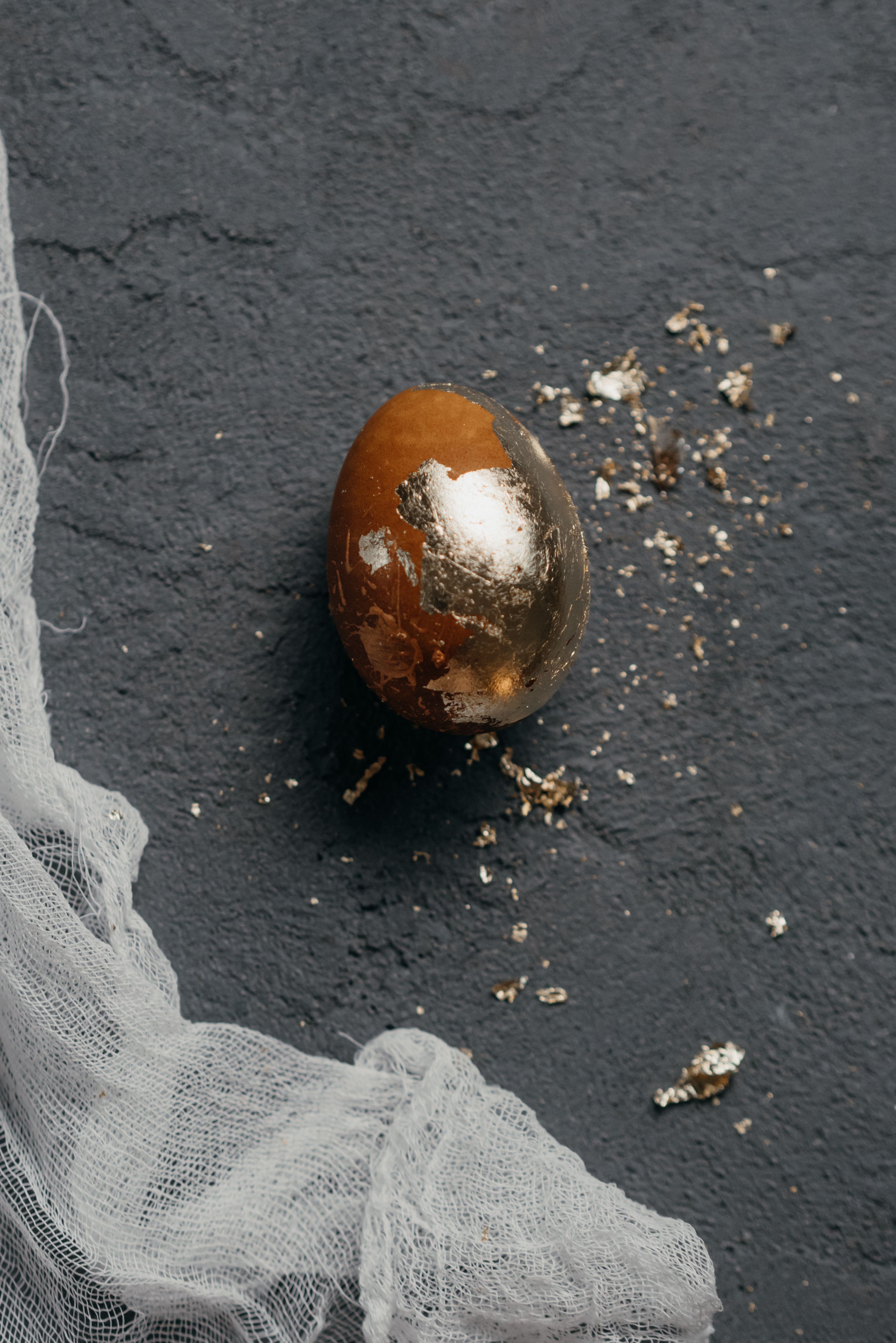 A beautifully decorated golden Easter egg with foil details on a textured concrete background.