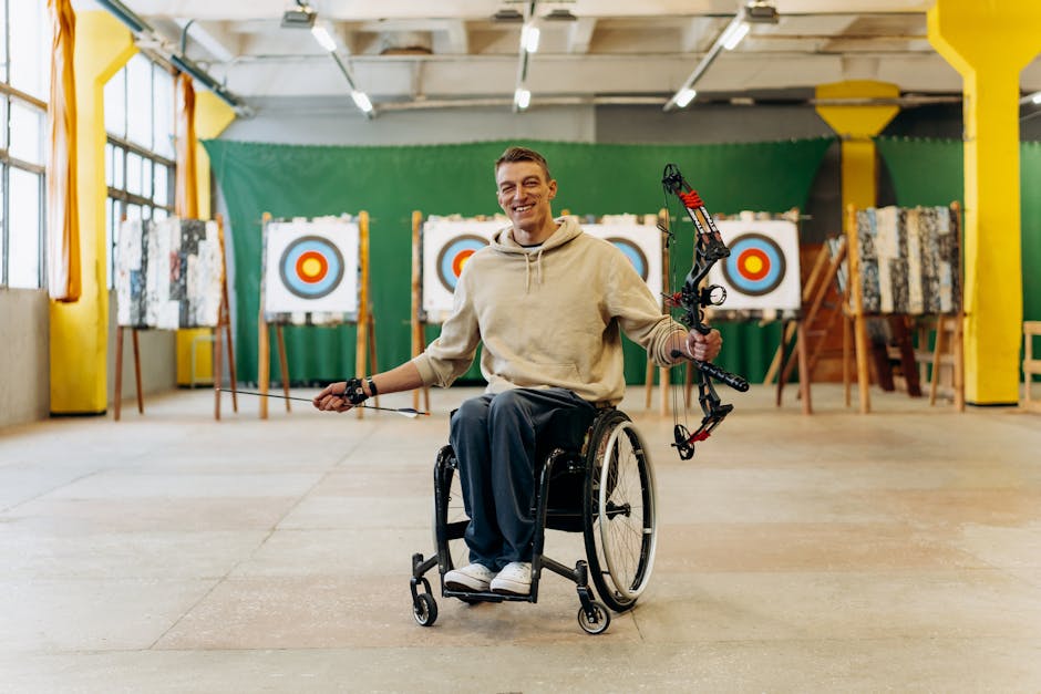 A disabled archer smiles while holding a bow in an indoor archery range.
