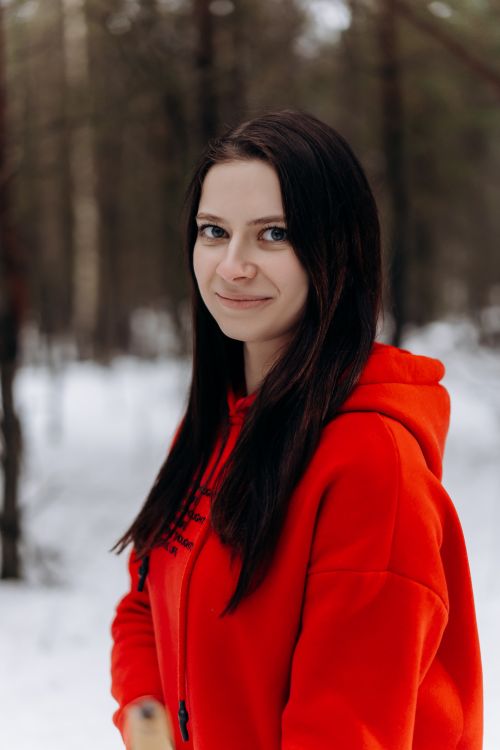 Free A young woman in a red hoodie smiles in a snowy forest setting, exuding warmth and vibrancy. Stock Photo