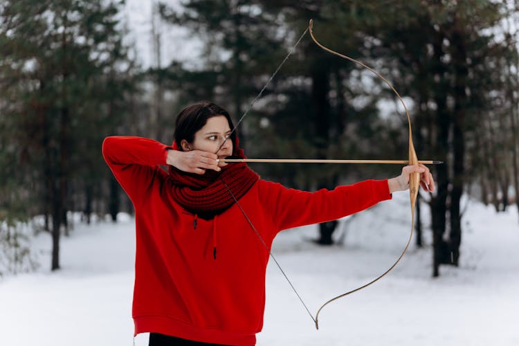 A Woman In A Red Hoodie Holding A Bow And Arrow 