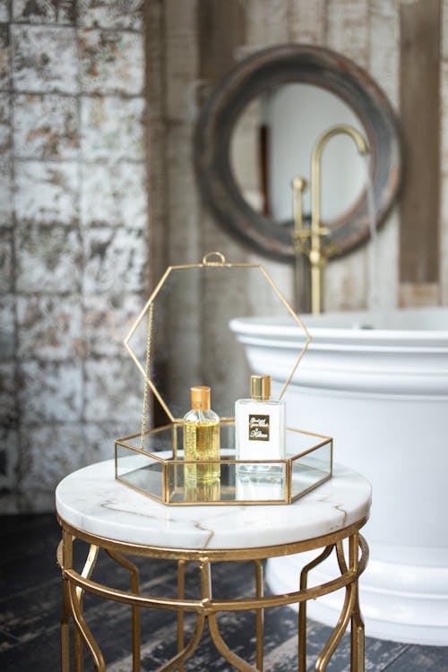 Glass box with bottles of spa supplies placed on round table near white bathtub in modern stylish bathroom with mirror