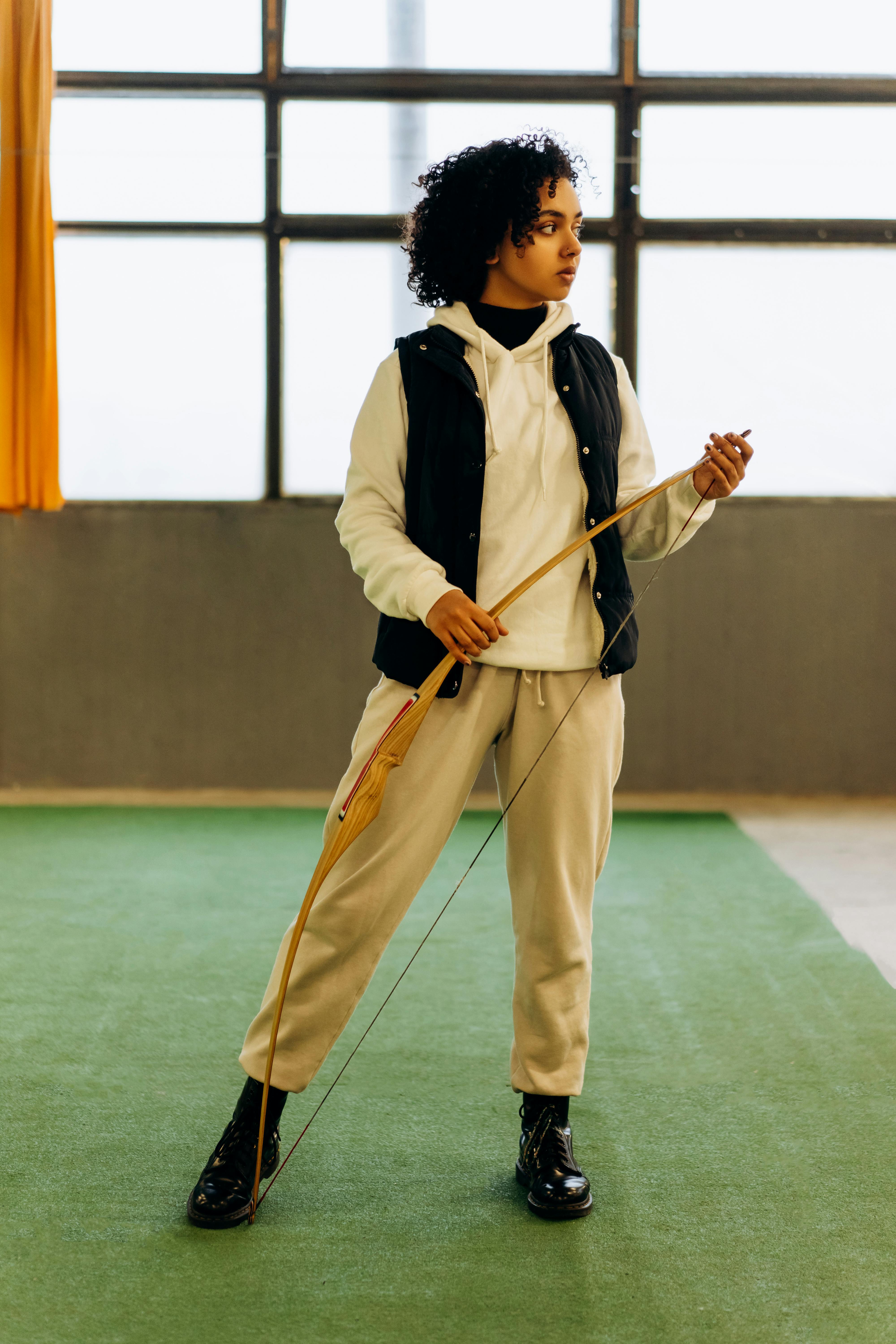 A young woman stands indoors holding a bow, embodying focus and strength.