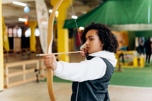 Young woman concentrating while practicing archery indoors. Perfecting her aim with determination.