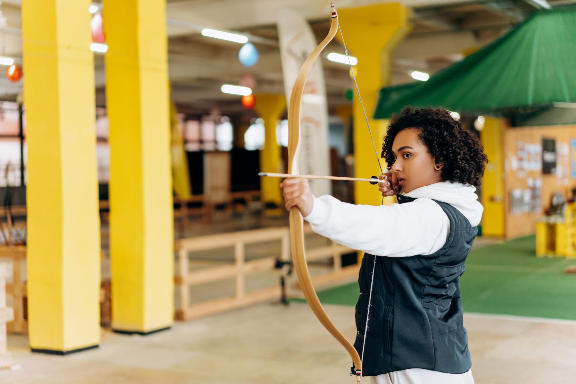 A woman aiming a bow indoors, showcasing precision and concentration in an archery practice session.