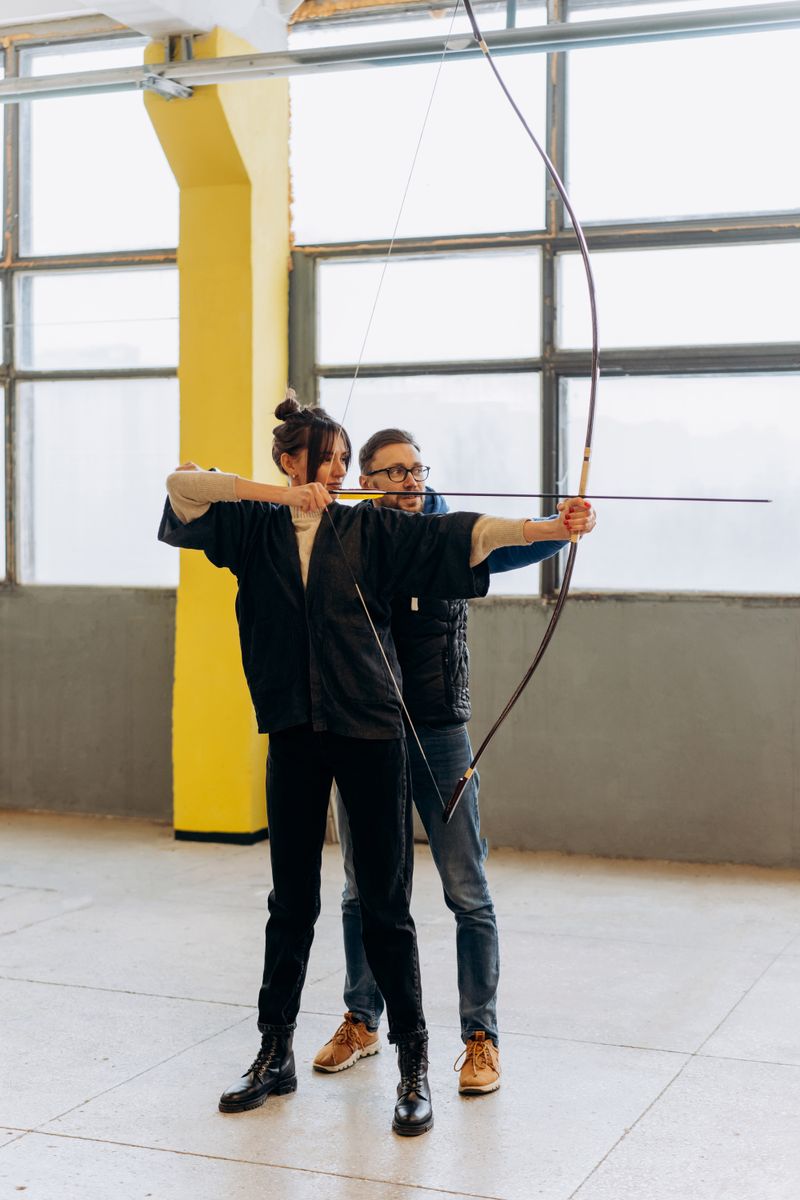 Woman receiving archery instructions indoors, focusing on aim and technique.