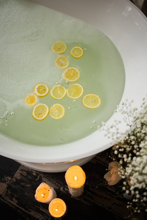 Free From above of white tub with clear water near burning candles and blooming flowers in modern bathroom during skincare treatment Stock Photo