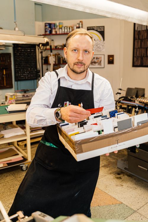 Free Man in a print shop holding a box of cards, wearing an apron and white shirt. Stock Photo