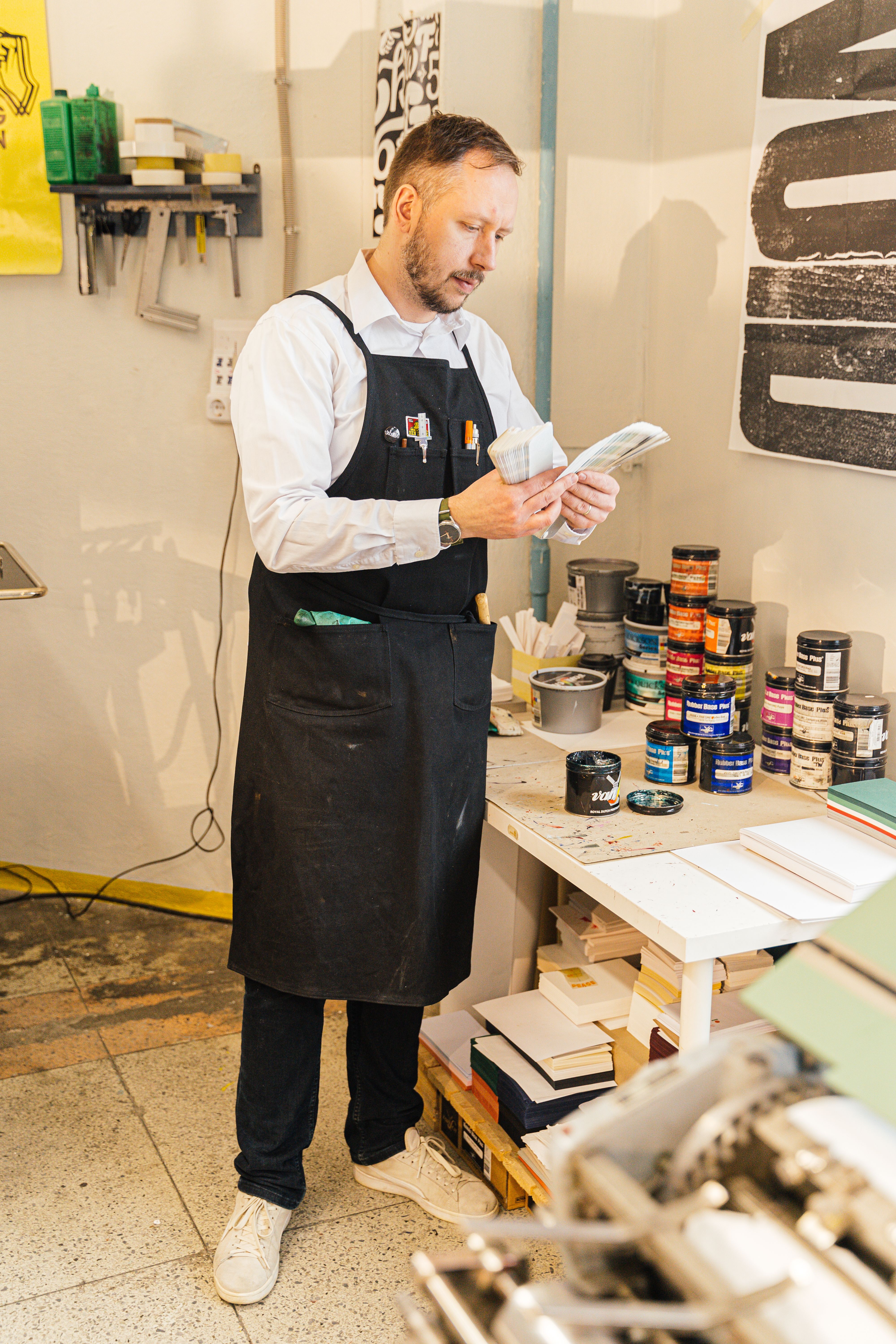 A graphic designer stands in a studio, examining supplies. Creative workspace setting.