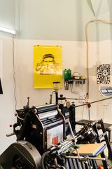 Printing press in a studio with a yellow poster on the wall