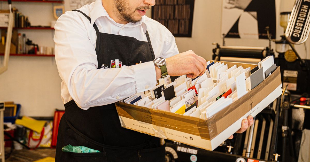 Adult man organizing cards in an industrial print workshop, wearing apron and focused on work.