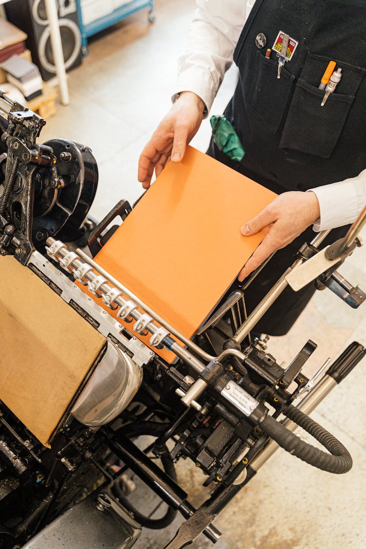 High Angle View Of A Man Putting Orange Paper Into Binding Machine