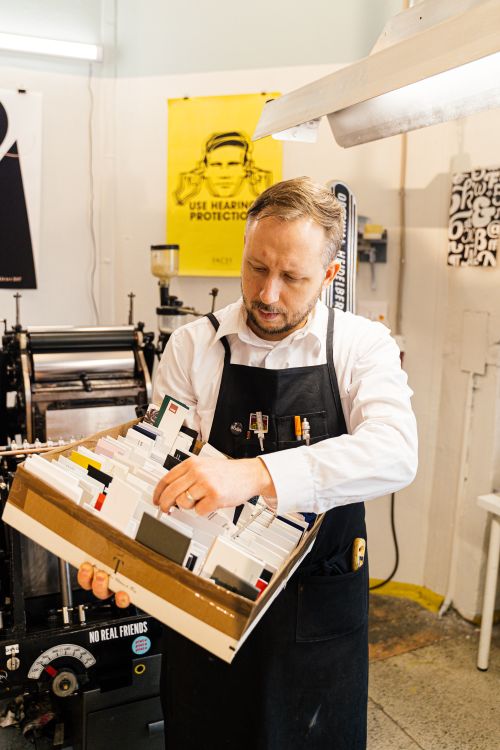Free Adult man organizing printing supplies in a workshop with industrial machines around him. Stock Photo