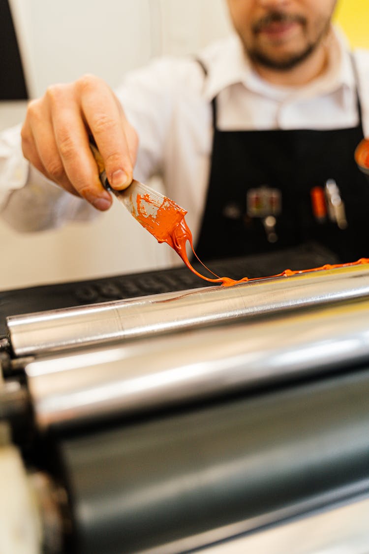 Man Applying Red Paint Onto Metal Press