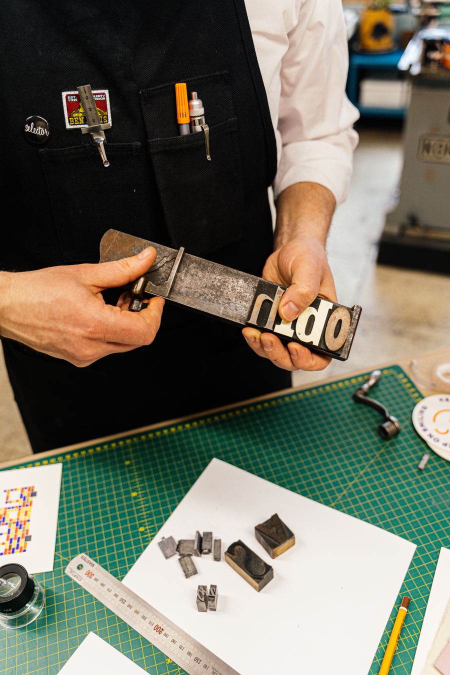 Man in workshop holding a typography block, showcasing craft and design skills.