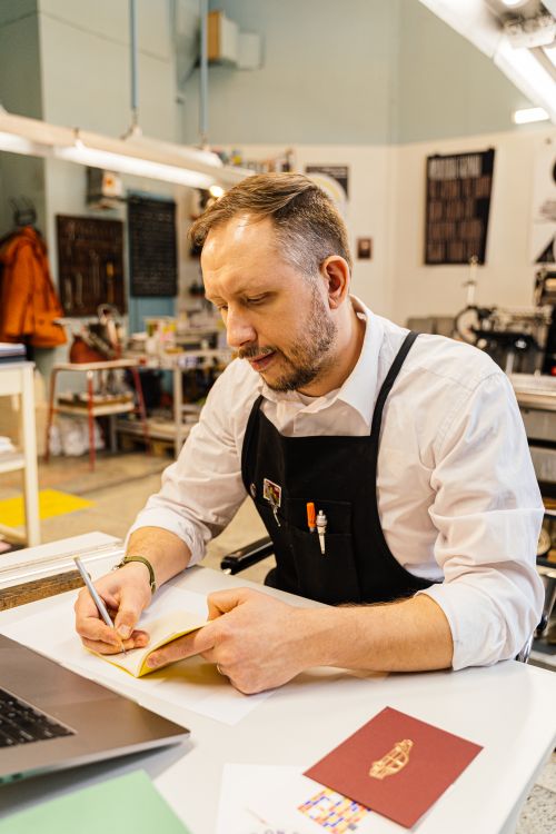 Free Man wearing black apron taking notes in creative studio setting. Stock Photo